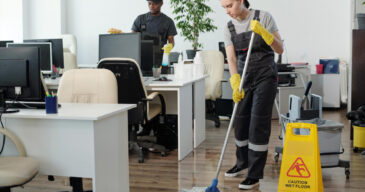 young-black-man-wiping-computer-monitors-while-woman-with-mop-cleaning-floor