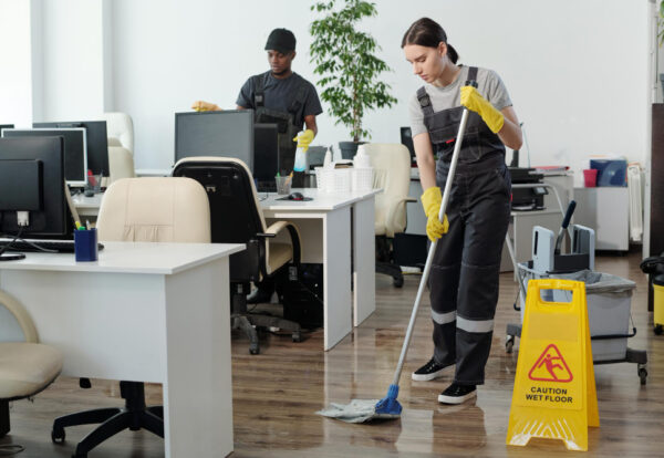 young-black-man-wiping-computer-monitors-while-woman-with-mop-cleaning-floor